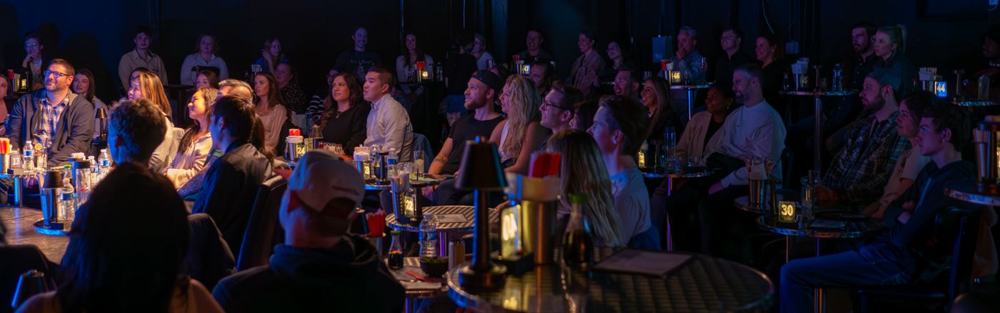 a group of people sitting at tables laughing watching comedy