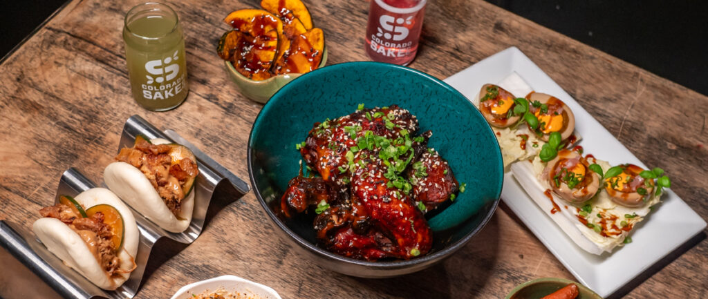 a bowl of chicken wings with sauce and vegetables with 2 glasses of sake