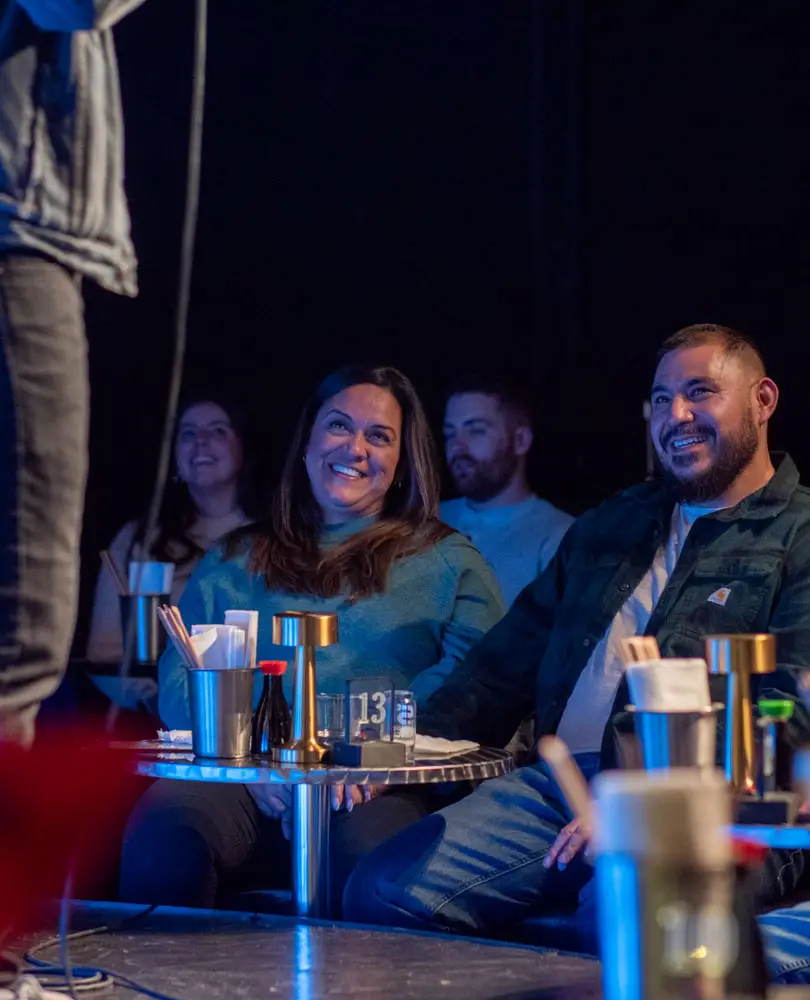 a group of people sitting at a table laughing at comedy